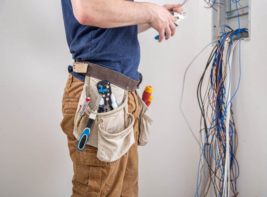 Electrician with tool belt working on a wall panel full of wires.
