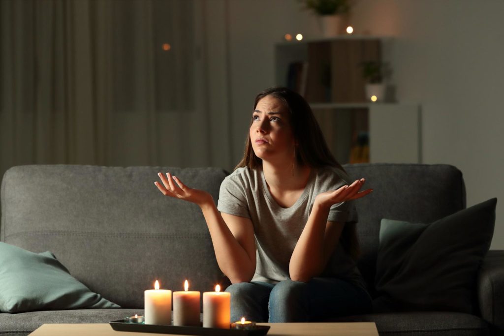 Woman sitting on a couch with candles during a power outage, looking confused.