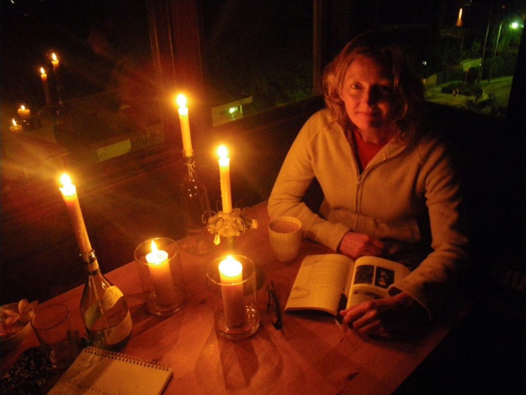 Woman reading a book at a table lit by multiple candles during a blackout.