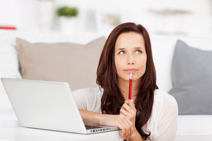 Woman sitting with a laptop, holding a pen to her chin while thinking.