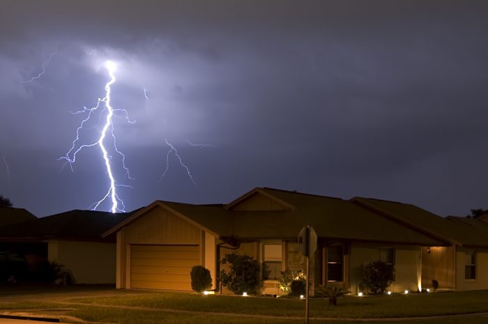 Lightning bolt striking near a residential house during a thunderstorm.