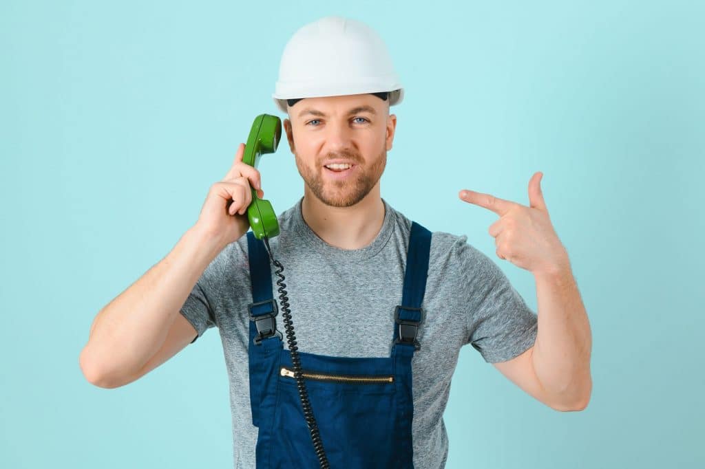 Smiling construction worker in a hard hat talking on a green corded phone.